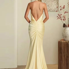 Woman wearing a light yellow evening gown with an open back, standing in a room with a neutral color scheme.