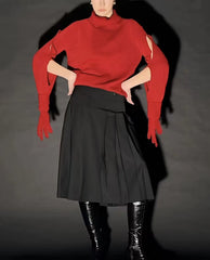 Person wearing a red sweater and black skirt with black boots on a dark background