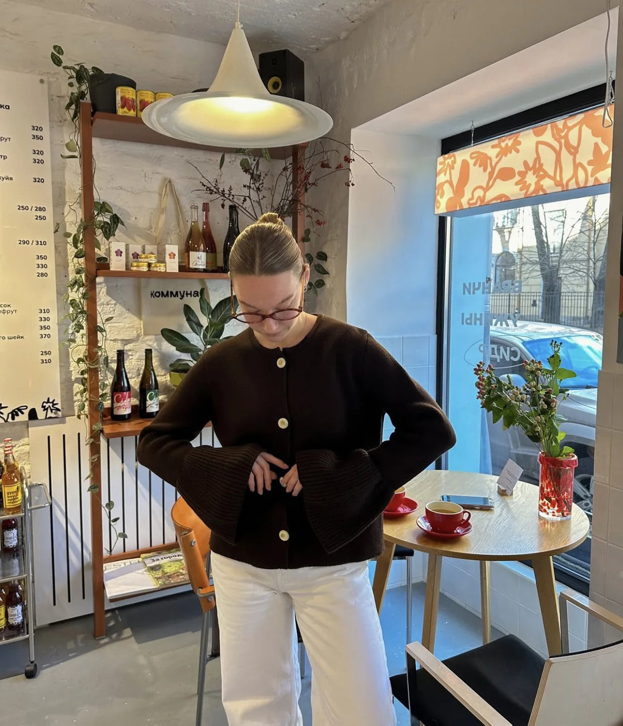 Woman in a brown sweater standing in a cafe with a menu board and decor in the background