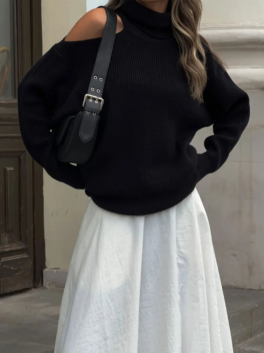 Person wearing a black sweater and white skirt with a black bag.