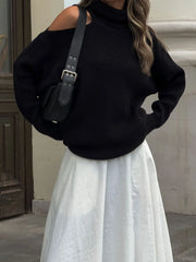 Person wearing a black sweater and white skirt with a black bag.