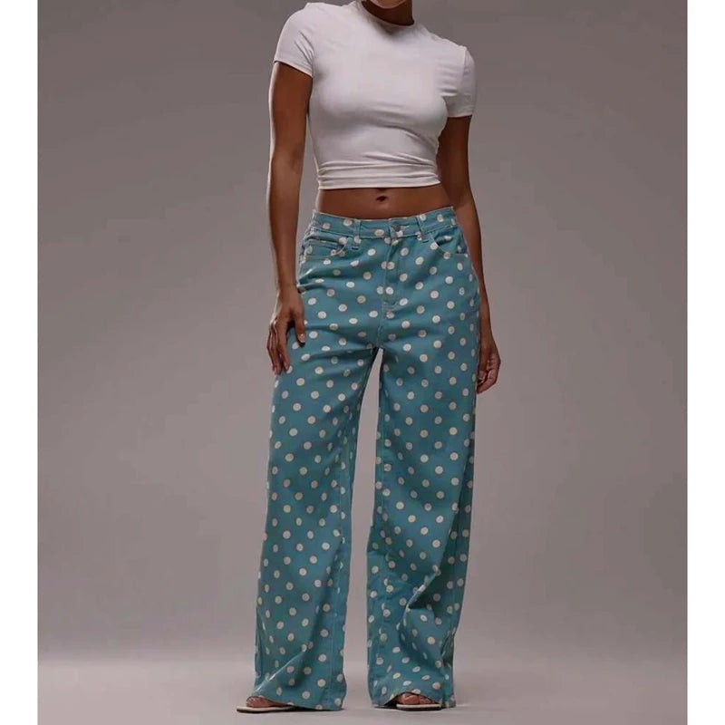 Person wearing teal pants with white polka dots and a white top on a gray background