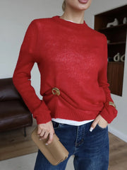 Person wearing a red sweater with a gold button, holding a beige clutch in a room.