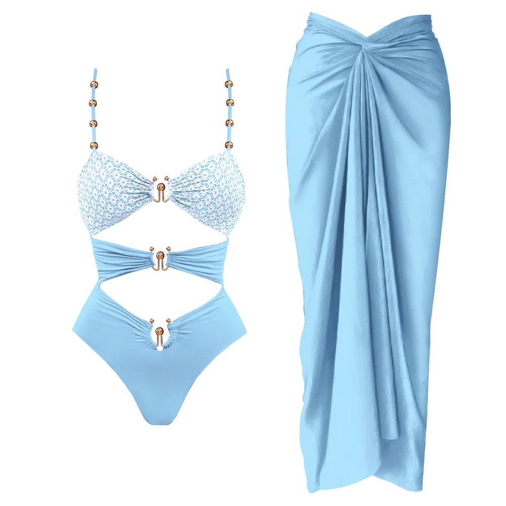 Light blue cutout one-piece swimsuit with embellished straps and matching draped cover-up skirt.