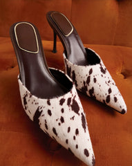 Brown and white cow print stiletto heels on an orange couch