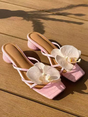 Pink high-heeled sandals with white orchid decorations on a wooden surface
