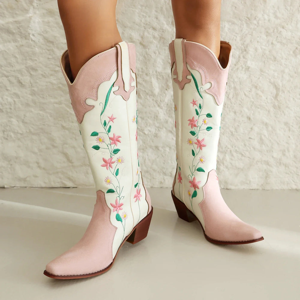 Pink and white cowboy boots with floral embroidery on a neutral background