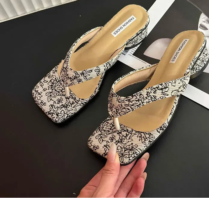 Pair of floral-patterned high-heeled shoes on a black surface with a magazine underneath.