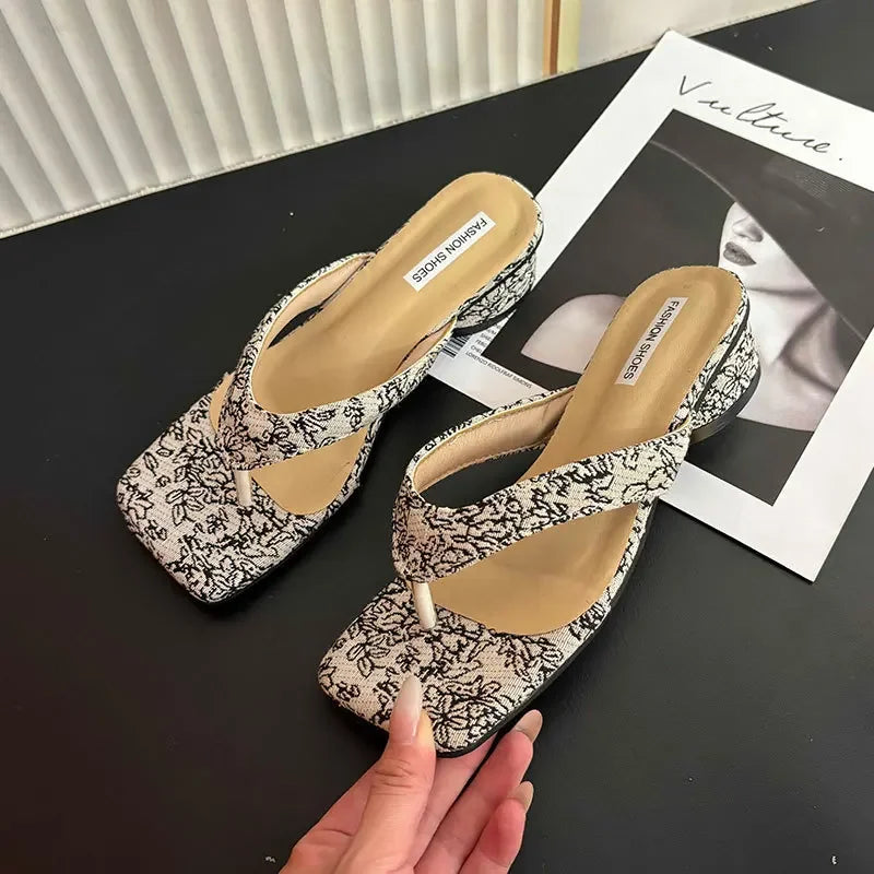 Pair of floral-patterned high-heeled shoes on a black surface with a magazine underneath.