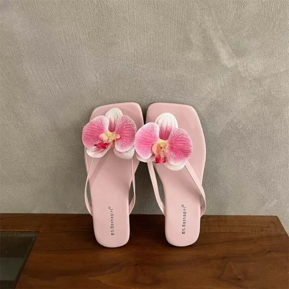 Pink flip-flops with orchid flowers on a wooden surface and gray background