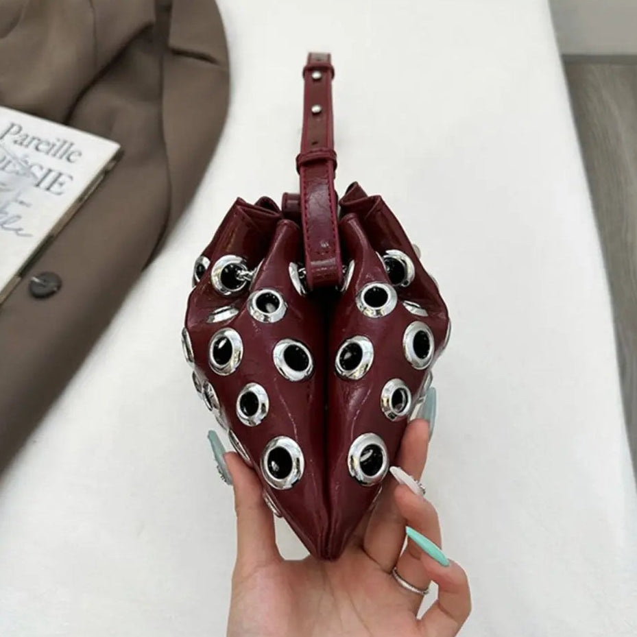 Heart-shaped bag with eye-like embellishments held by a hand on a white surface.