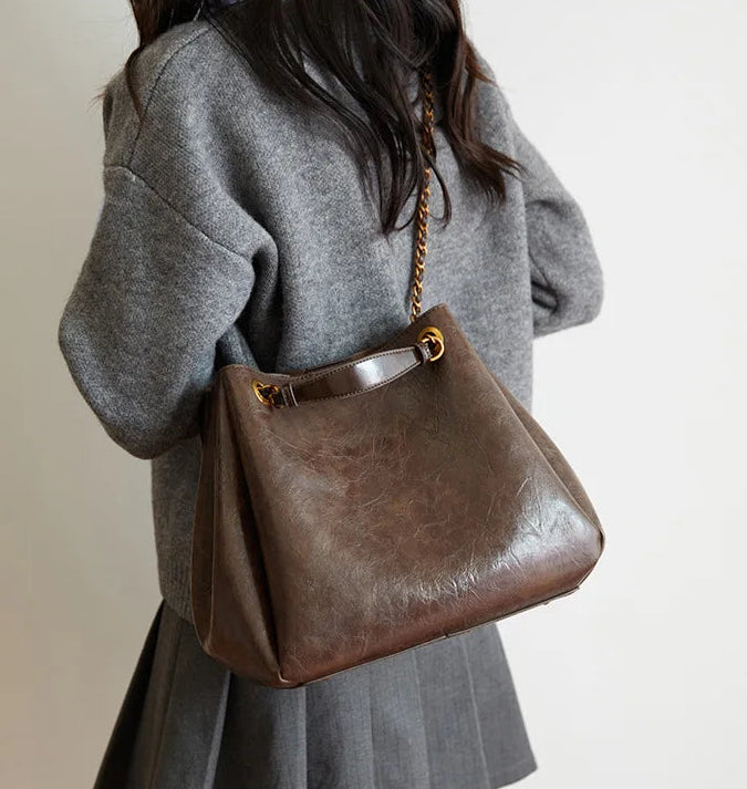 Person wearing a gray coat holding a brown leather handbag with a gold chain strap.