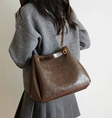 Person wearing a gray coat holding a brown leather handbag with a gold chain strap.