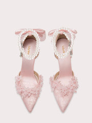 Pink high-heeled shoes with floral decorations and bow details on a white background