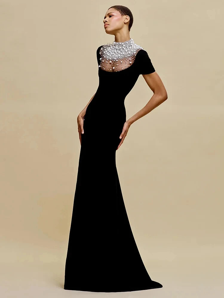 Woman wearing a black evening gown with a beaded neckline on a beige background