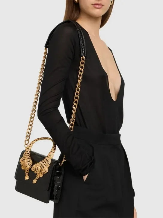 Woman wearing a black top and holding a black crocodile effect top handle bag with gold tiger sculptures
