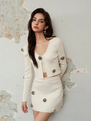 Woman wearing a cream-colored outfit with decorative buttons against a textured wall.