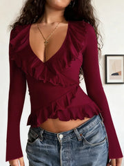 Woman wearing a burgundy ruffled top with long sleeves and blue jeans.
