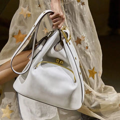 White handbag with gold accents held by a person wearing a star-patterned dress.