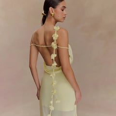 Woman wearing a light yellow dress with floral details on a soft pink background