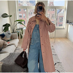 Person taking a mirror selfie wearing a checkered coat and denim overalls in a living room.