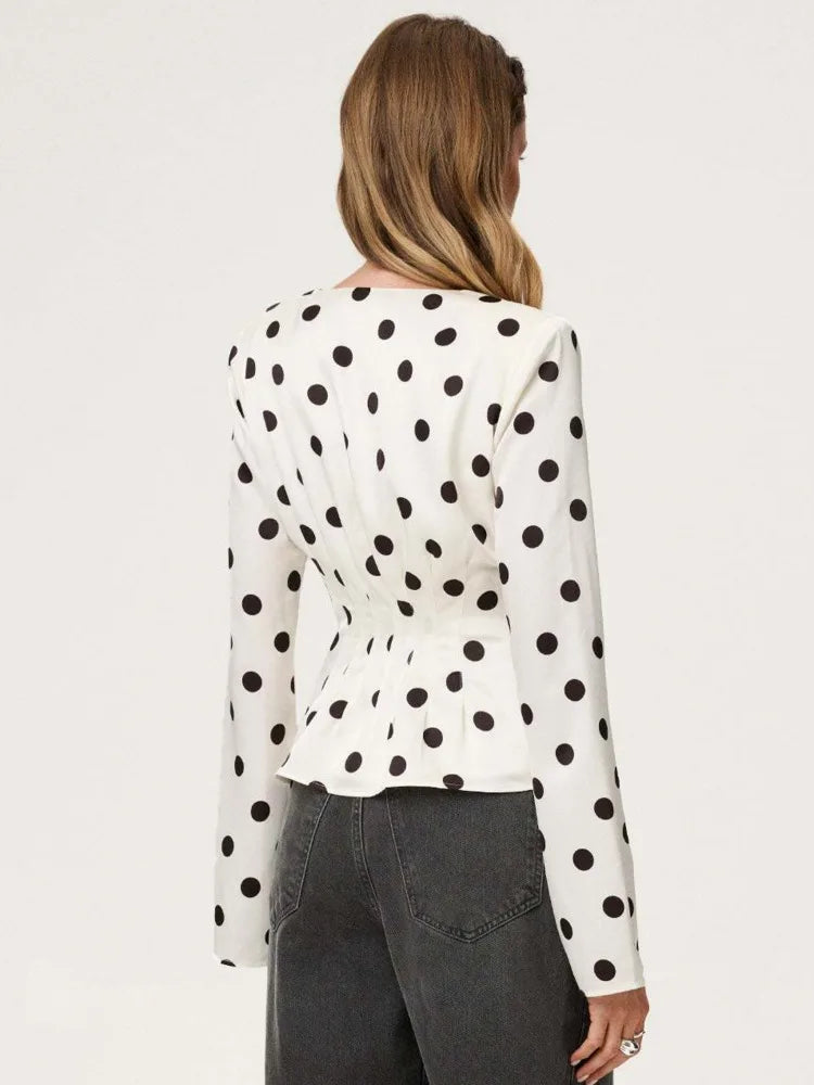 Woman wearing a white blouse with black polka dots and gray pants on a white background