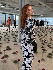 Woman in a black and white floral dress standing in an indoor setting with flowers on the floor.