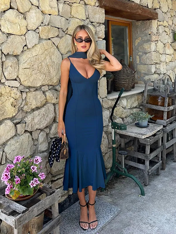 Woman in a blue dress standing in front of a stone wall with a rustic setting.