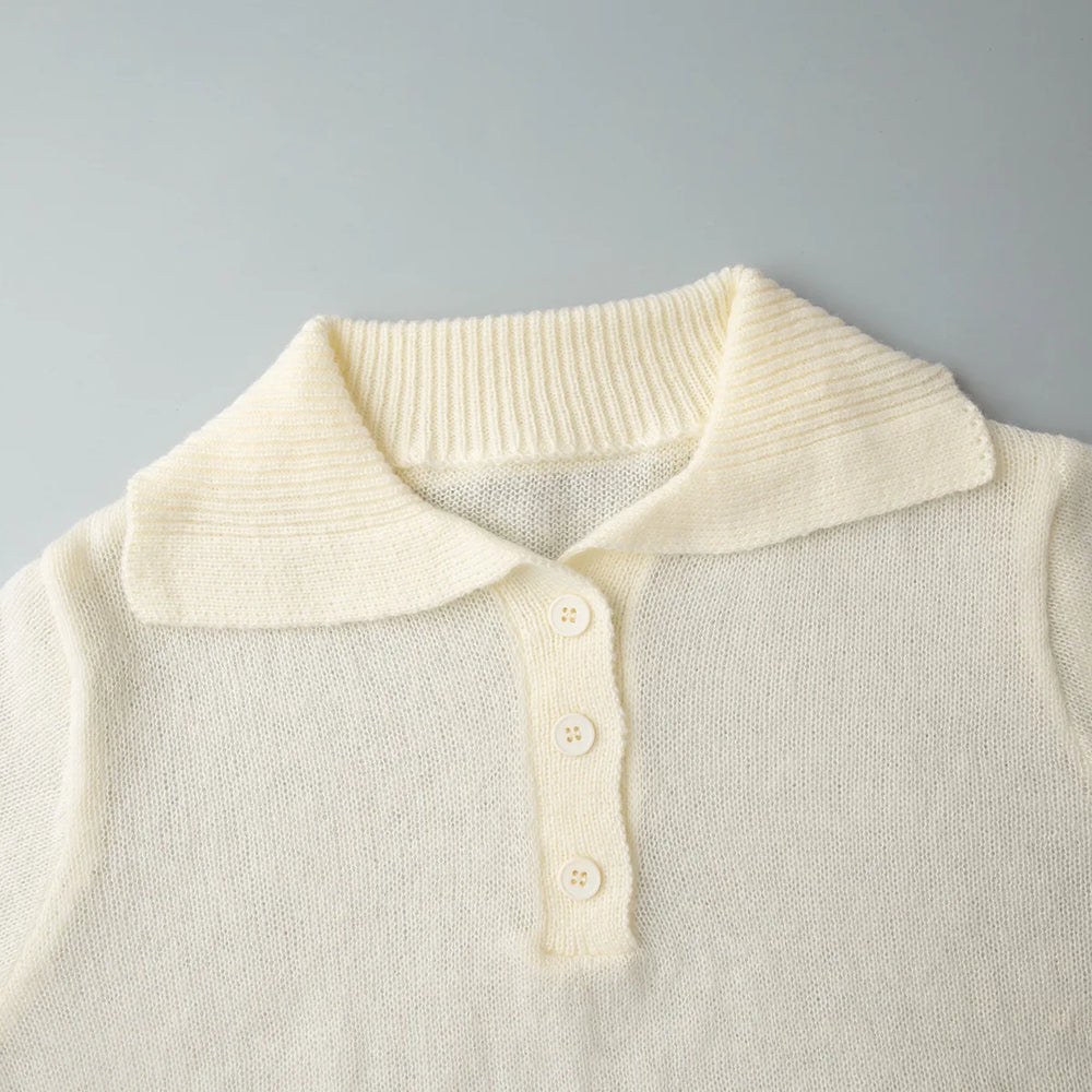 Close-up of a cream-colored top with a collar and buttons on a grey background