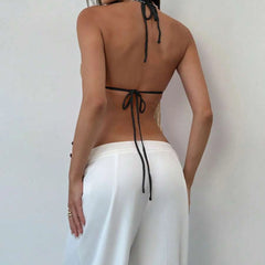 Person wearing a black halter top and white pants against a plain background