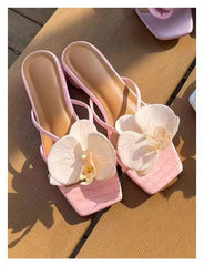 Pink high-heeled shoes with white flowers on a wooden surface