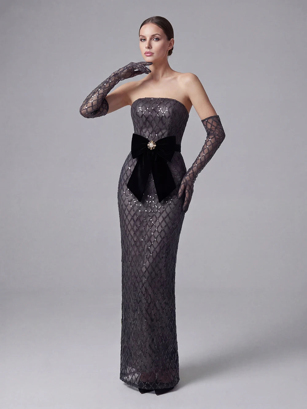 Woman wearing a black lace evening gown with a large bow on a gray background