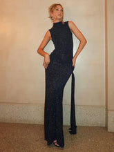 Woman wearing a long dark blue dress against a plain wall.