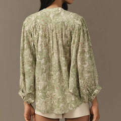 Green floral blouse worn by a person on a brown background