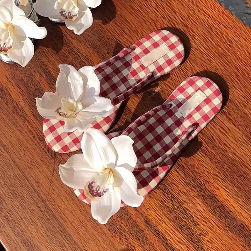 Red and white checkered slippers on a wooden surface with white flowers.