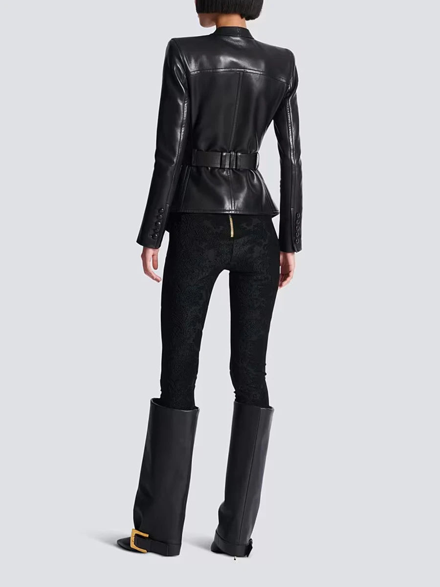 Person wearing a black leather jacket and pants with high boots on a light gray background