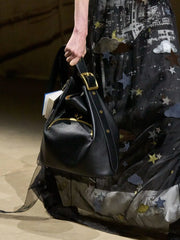 Black handbag with gold accents held by a person wearing a star-patterned dress.