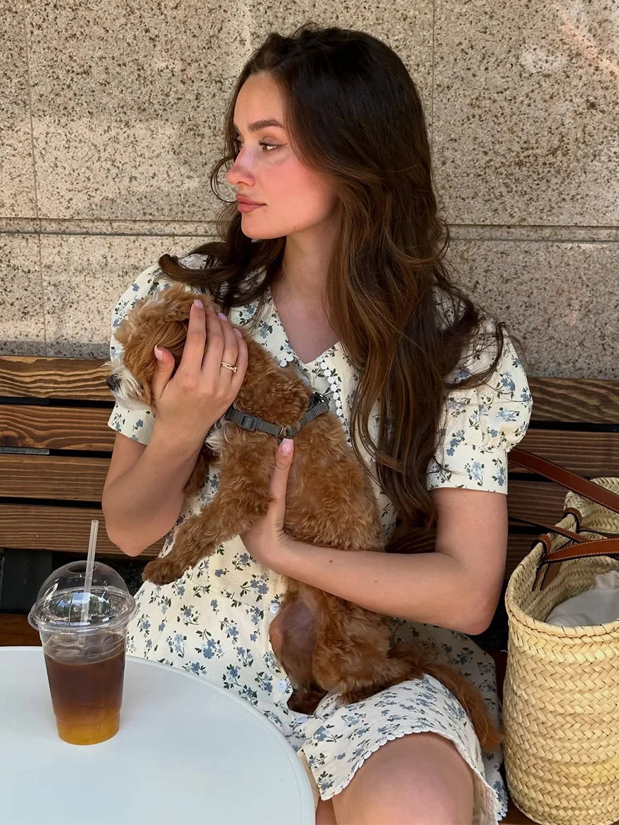 Woman holding a brown dog and a drink at an outdoor cafe.