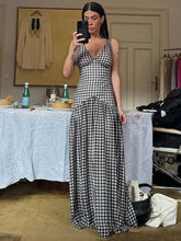 Woman taking a mirror selfie wearing a black and white checkered dress in a room with a table and various items.