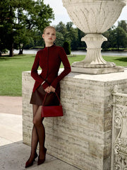 Woman in a red outfit standing next to a stone urn in an outdoor setting