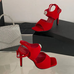 Red stiletto heels with rhinestone embellishment and ankle strap next to a silver handbag.