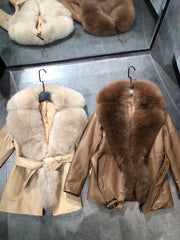 Two leather jackets with fur collars on hangers against a reflective surface.