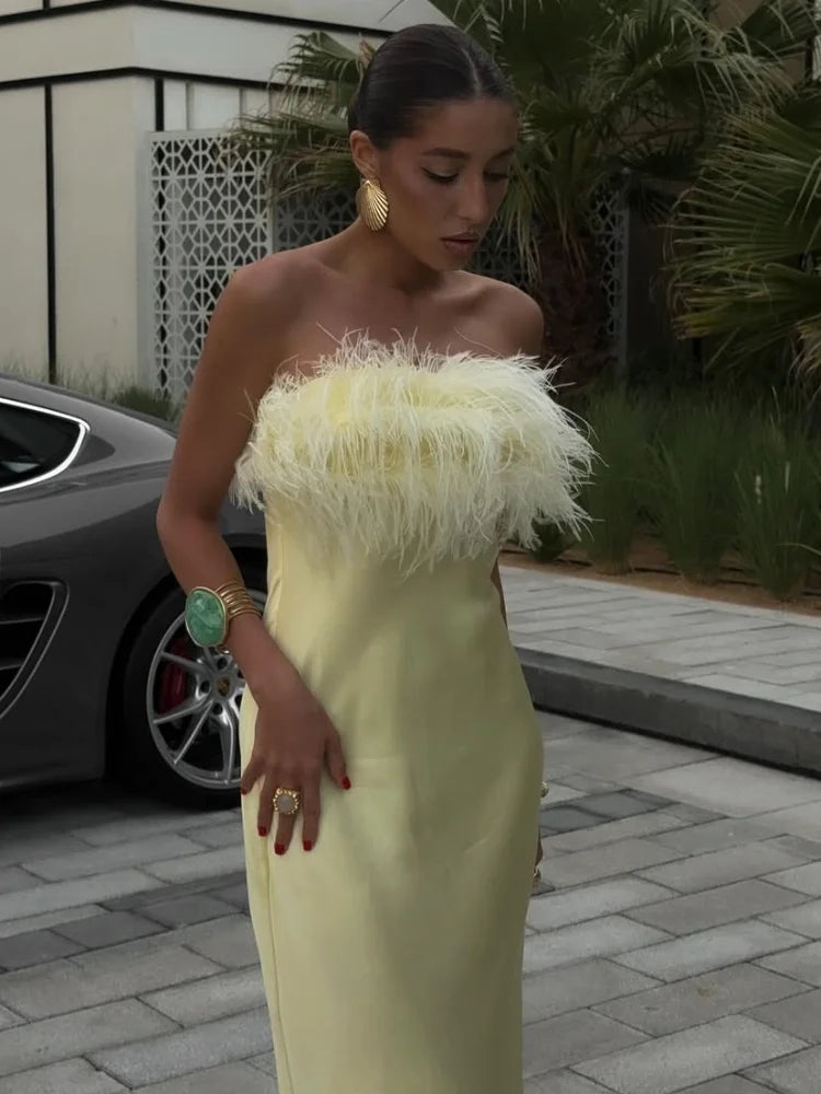 Woman in a strapless yellow dress with feather details standing outdoors.