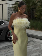 Woman in a strapless yellow dress with feather details standing outdoors.
