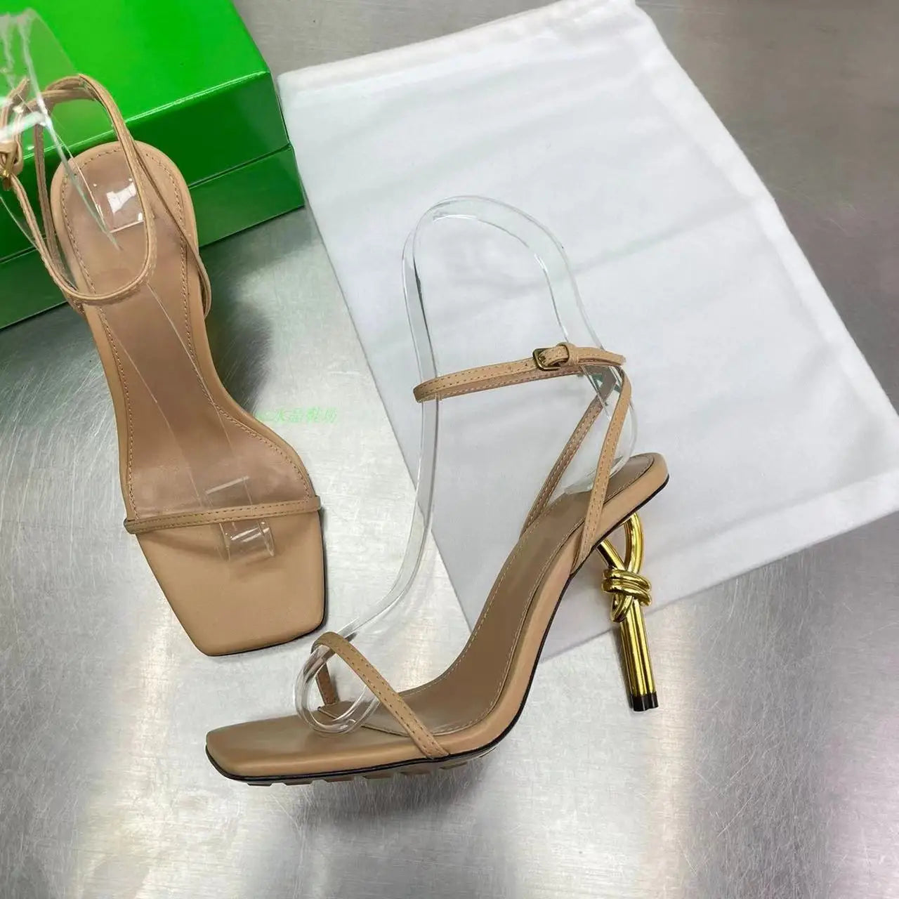 Beige high-heeled sandals with clear straps on a metallic surface.