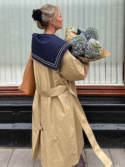 Trench coat with navy sailor collar and belt, held by a woman carrying flowers