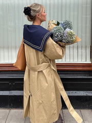Trench coat with navy sailor collar and belt, held by a woman carrying flowers
