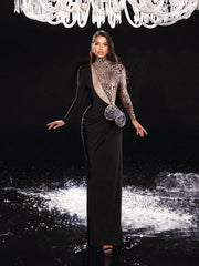 Woman in a black evening gown with a textured shawl and clutch, standing under a chandelier.
