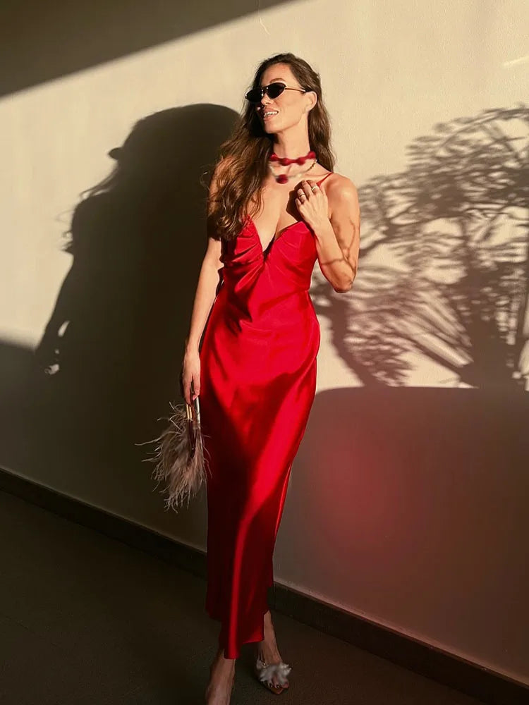 Woman in a red dress standing against a light-colored wall with shadows.