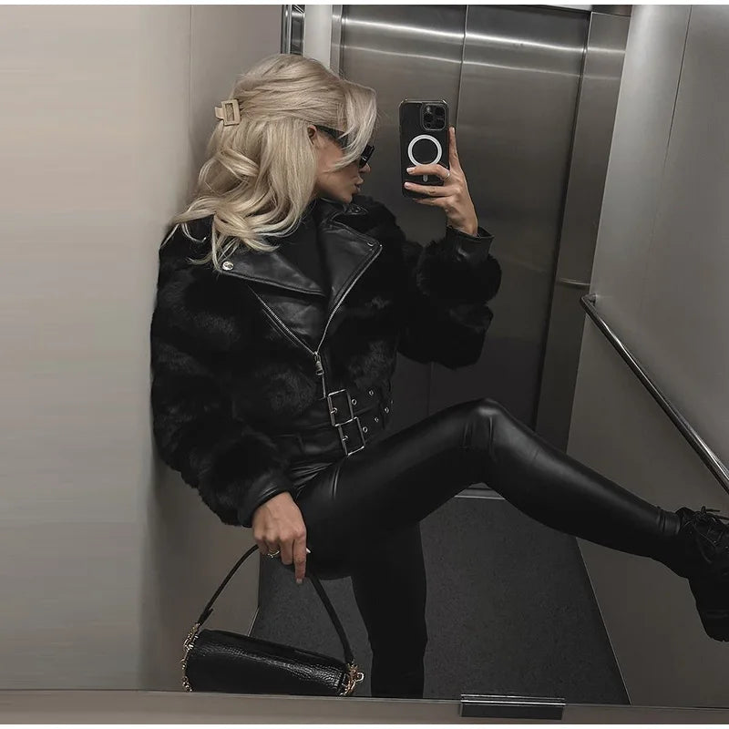 Woman in a black leather jacket and leggings taking a mirror selfie in an elevator.